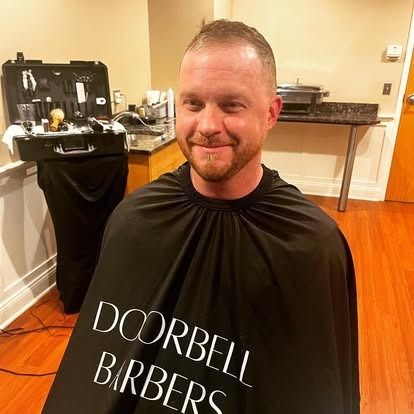 Smiling client in a Doorbell Barbers cape after a backstage haircut