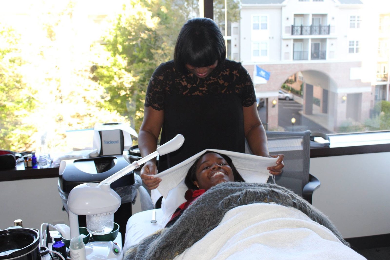 Esthetician giving a smiling employee an express facial with a warm towel in an office