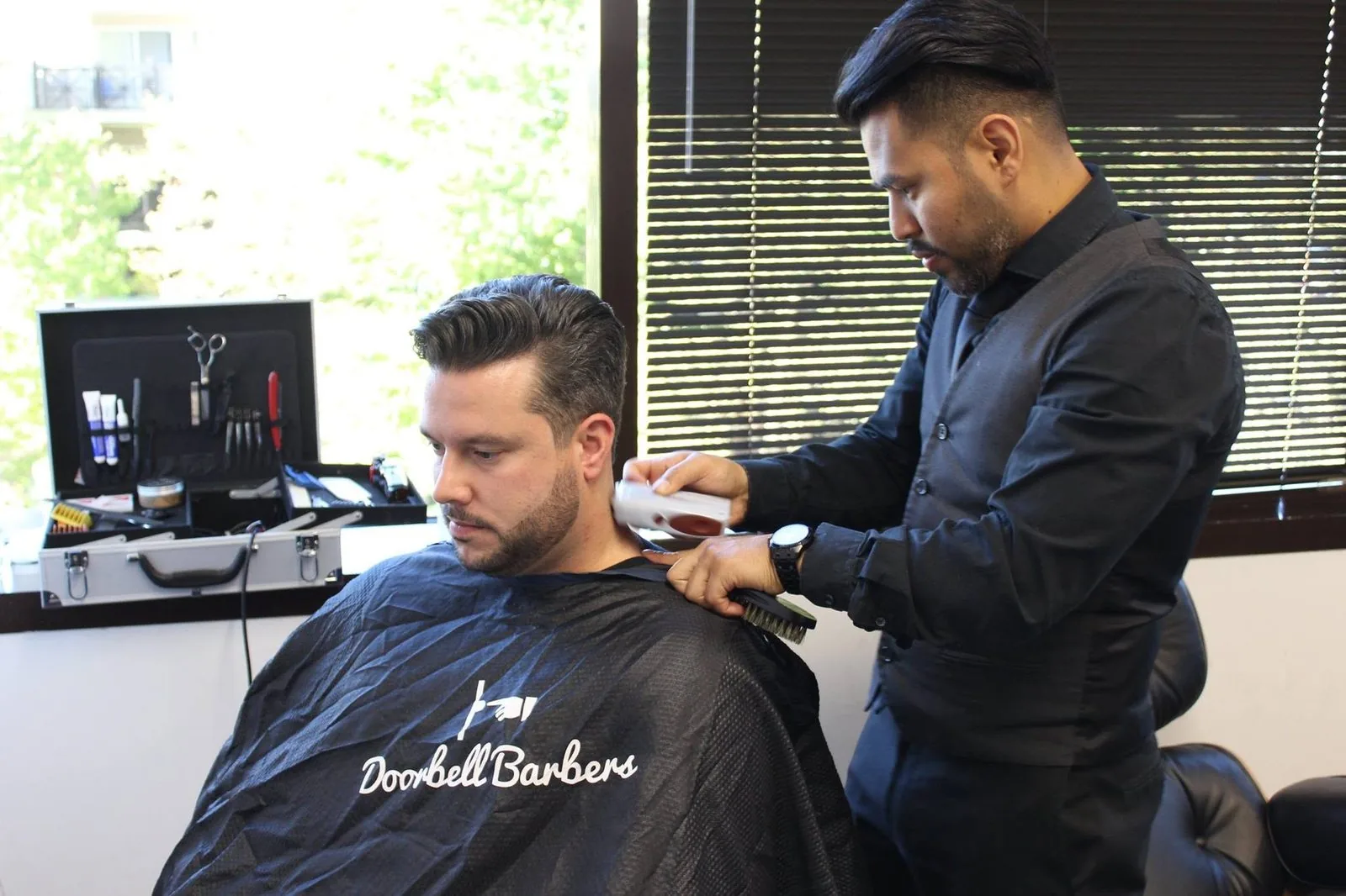 Doorbell barber giving an employee a haircut in a Doorbell Barbers cape during an office wellness day
