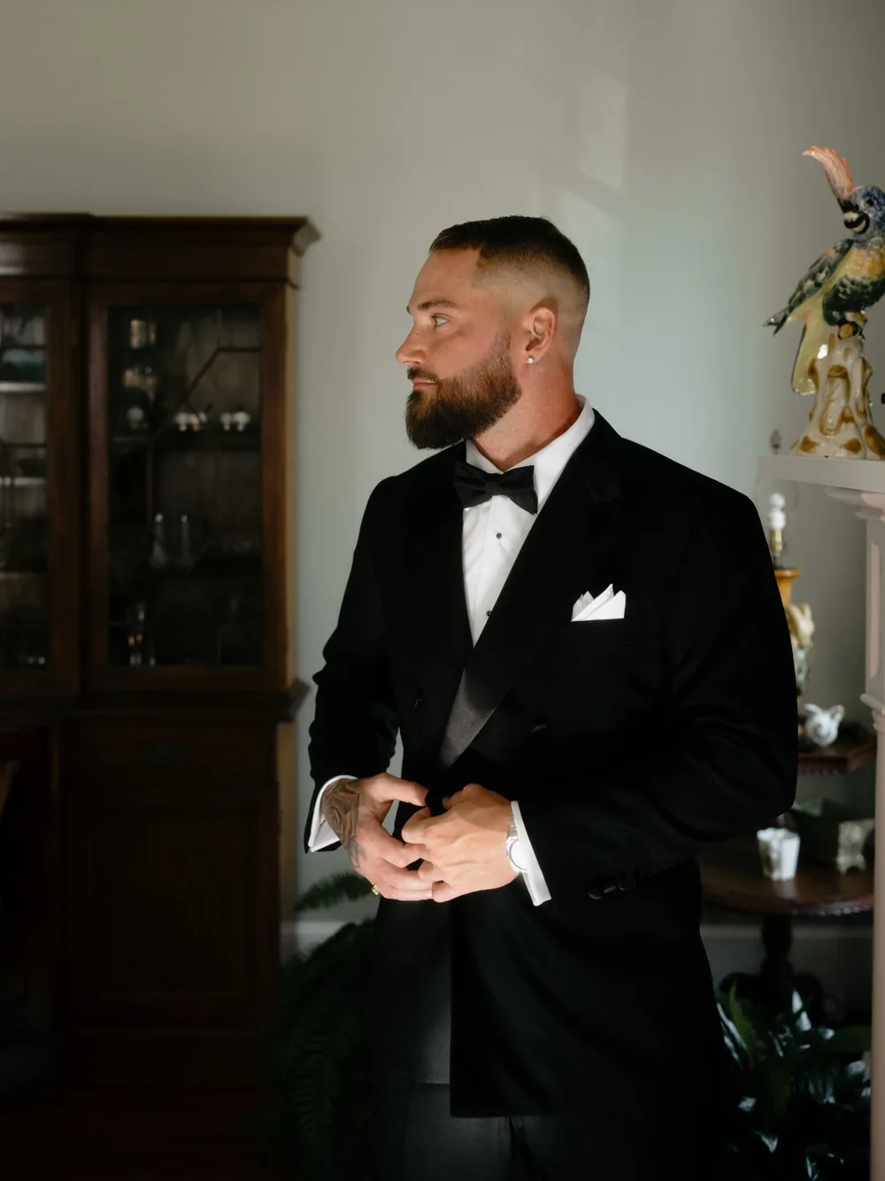 Groom with a skin fade and shaped beard buttoning his double-breasted tuxedo