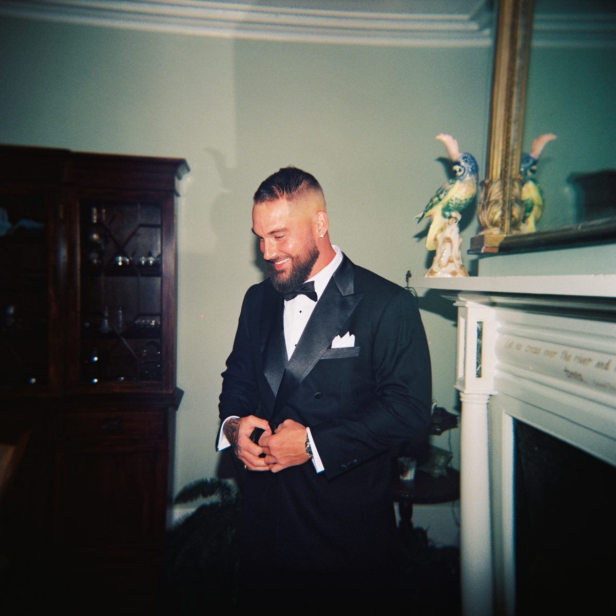 Groom with a fresh skin fade and groomed beard buttoning his tuxedo