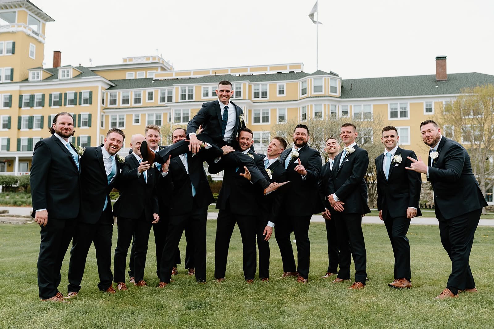 Groomsmen lifting the groom on the lawn of a New England wedding venue