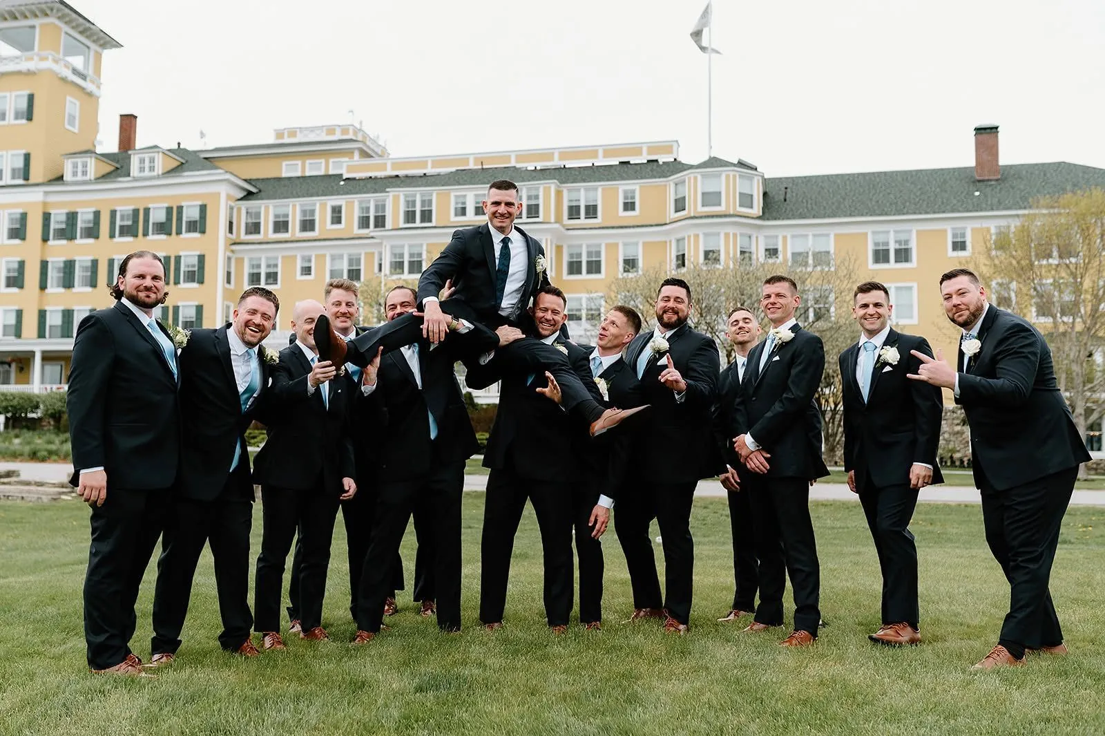 Groomsmen lifting the groom on the lawn of a New England wedding venue