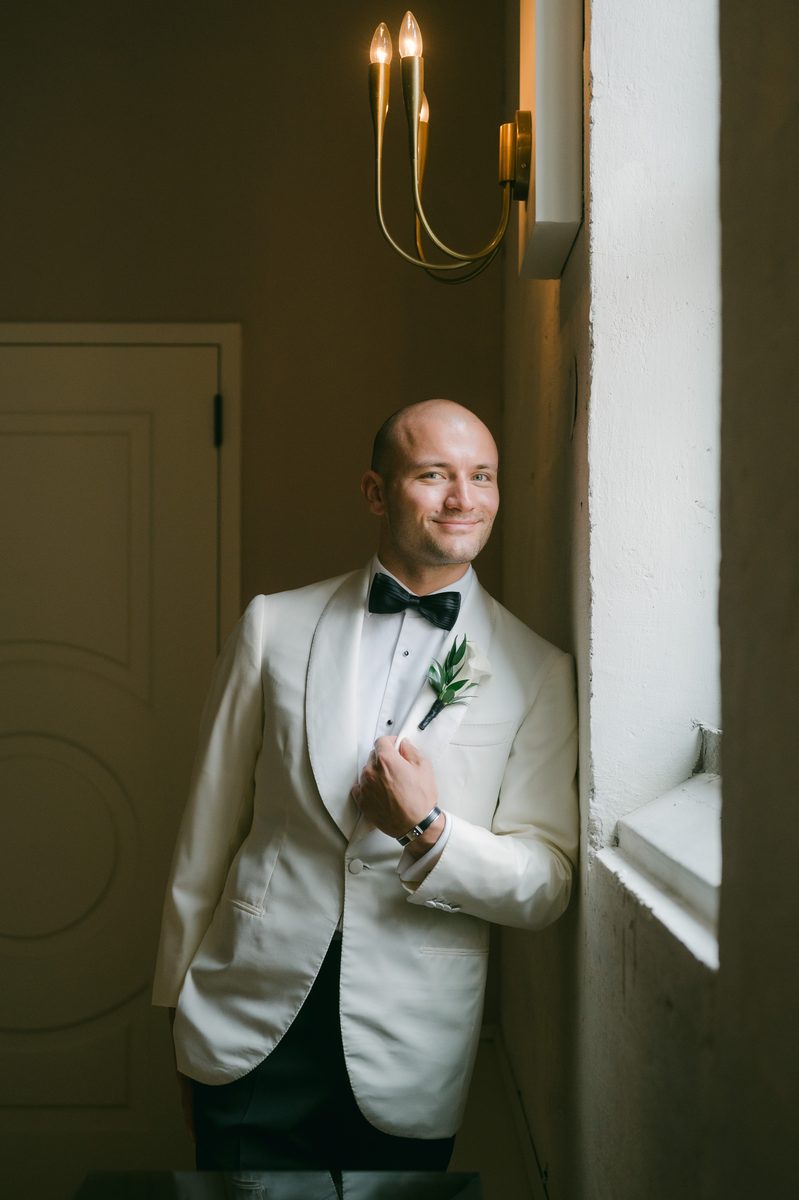 Groom in a white dinner jacket with a clean, freshly groomed look by a window