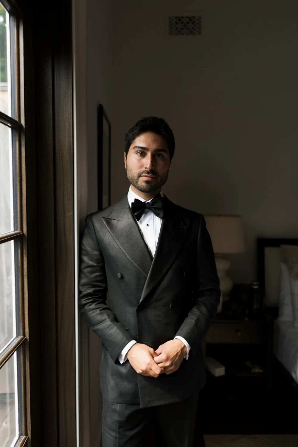 Groomsman in a double-breasted tuxedo by a window, freshly shaved and styled