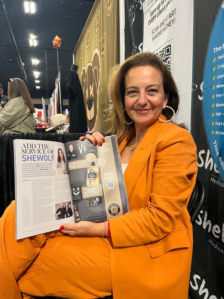 Semra Özcan, founder of Shewolf Medical, at a barber industry expo holding a magazine feature on Shewolf