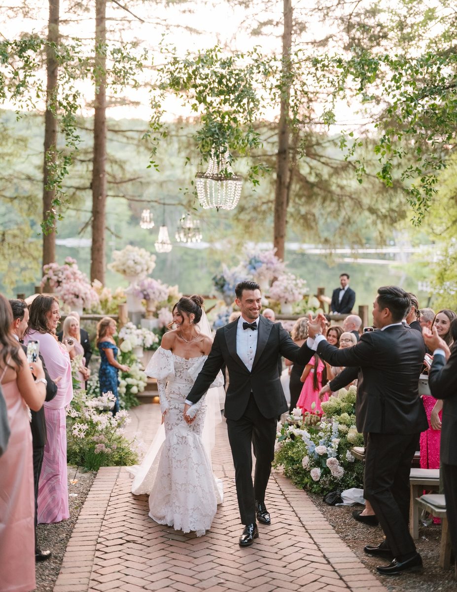 Newlyweds walking back down a flower-lined aisle after an outdoor ceremony